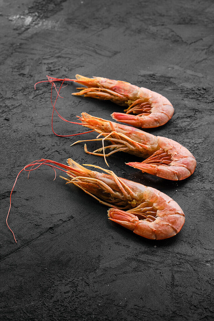 Three cooked prawns on a dark background