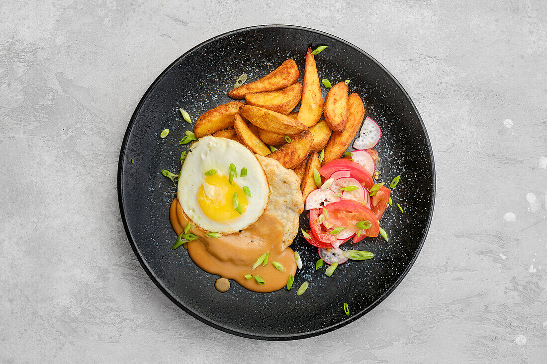 Top view of chopped pork sirloin with fried potato wedges, egg, fresh tomato and radish