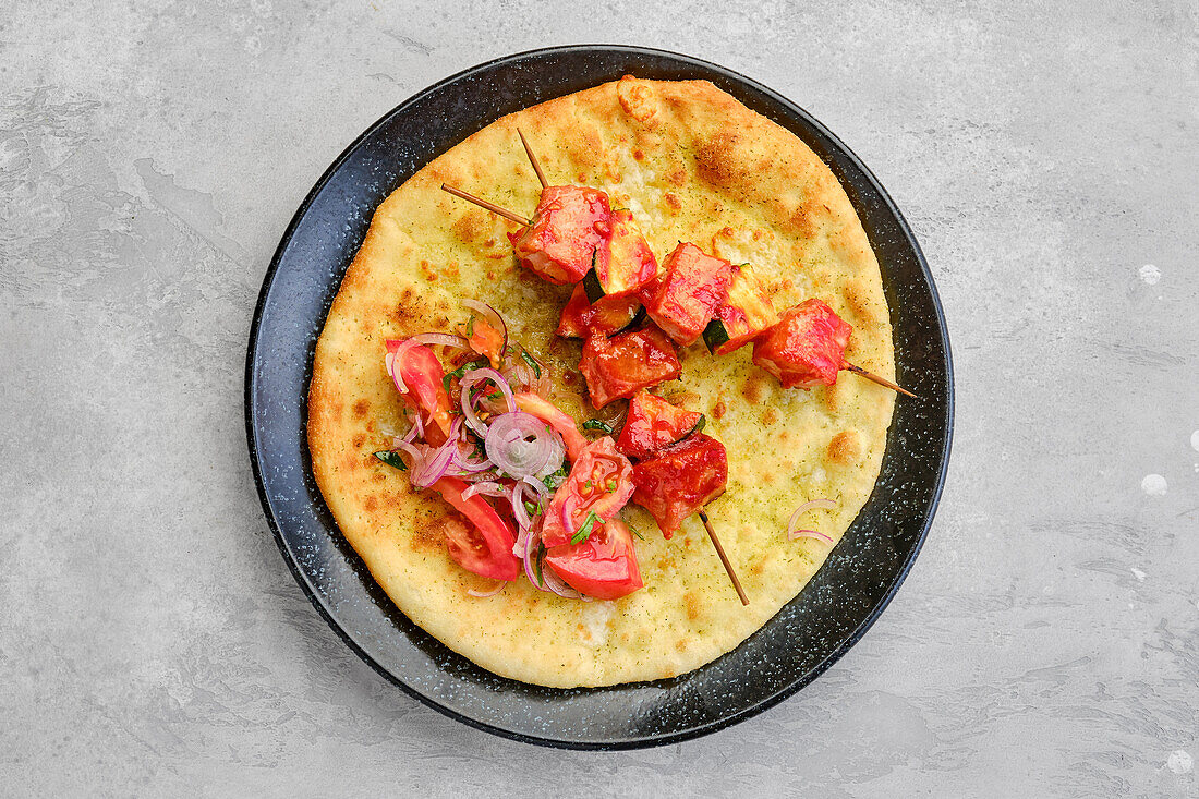 Shashlik skewers on flatbread with tomatoes and red onions