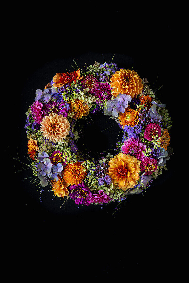 Floral wreath of dahlias, zinnias, hydrangeas and verbenas in orange, blue, purple and green