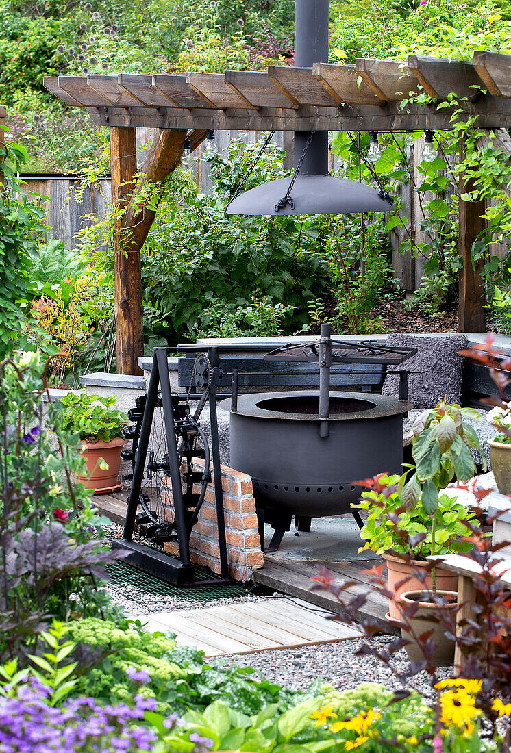 Feuerstelle unter Pergola im üppigen Garten mit Topfpflanzen