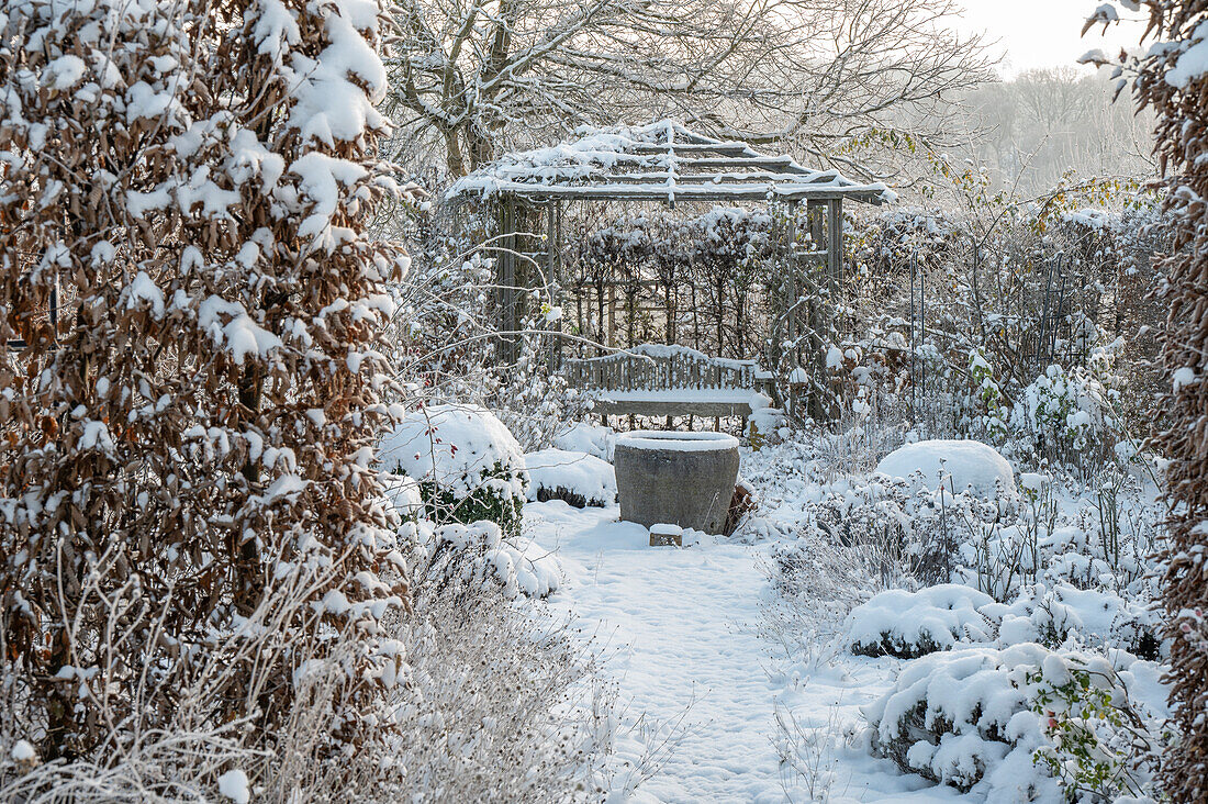 Verschneite Beete im winterlichen Garten und Pavillon mit Sitzplatz