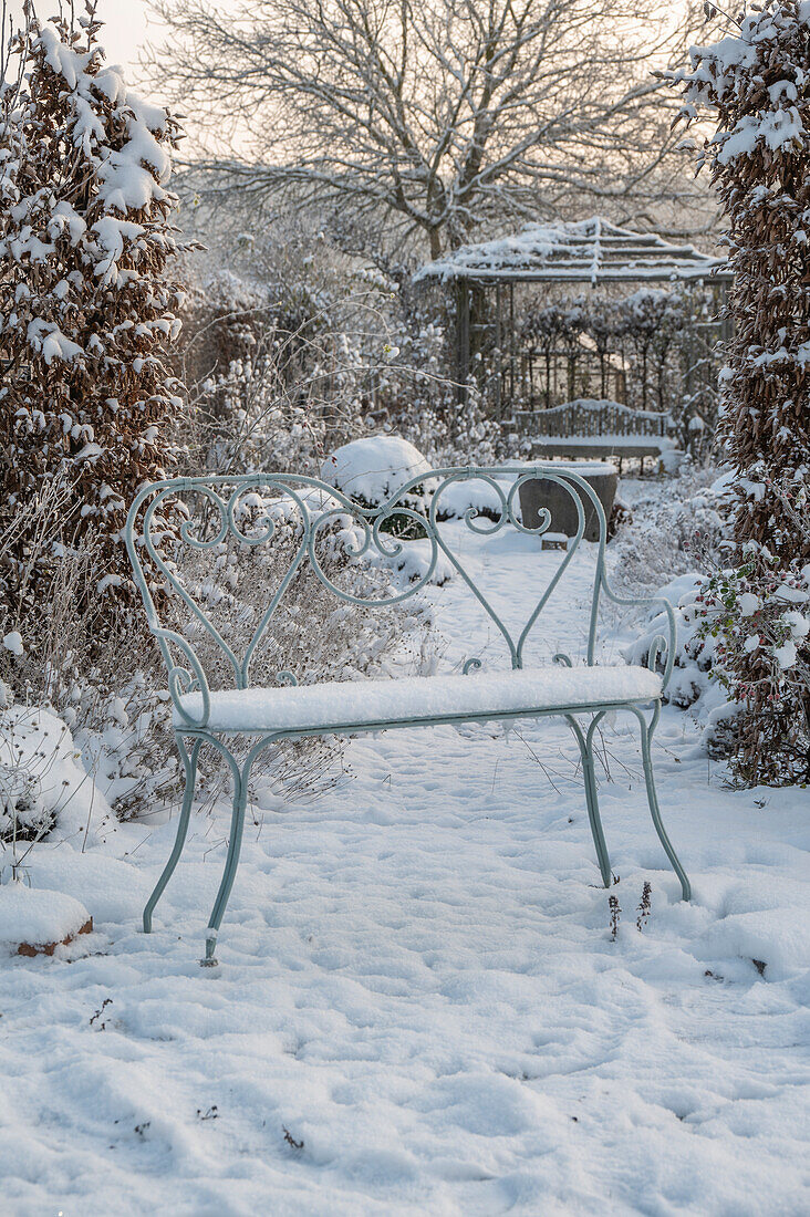 Verschneite Gartenbank im winterlichen Garten