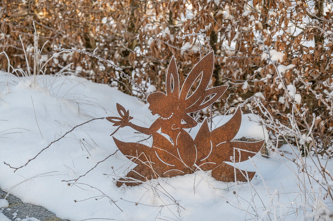 Verschneiter winterlicher Garten mit Elfenfigur im Schnee