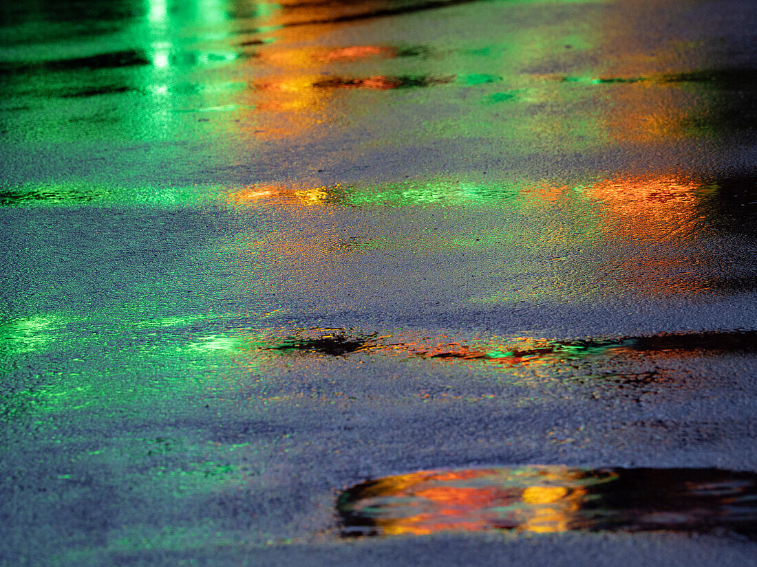 Lichter spiegeln sich in Pfützen auf Asphaltweg