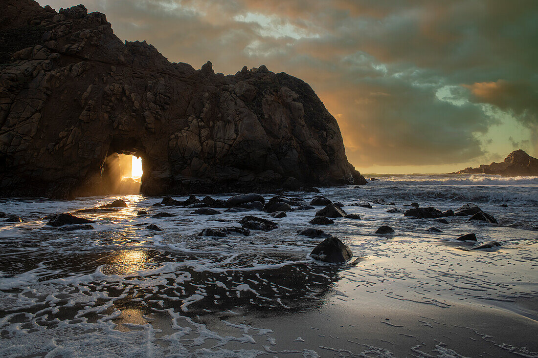 Sunset shines through a tunnel in this sea rock at Big Sur.