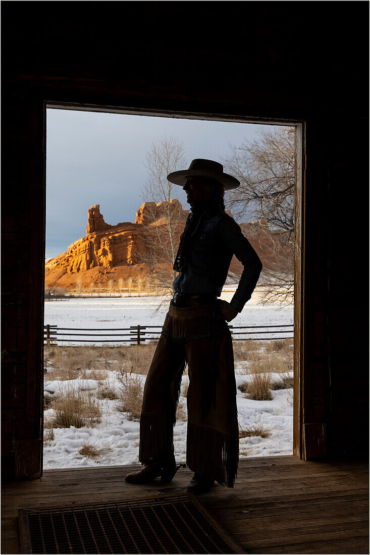 USA, Shell, Wyoming. Hideout Ranch with cowgirl silhouetted in doorway of log cabin. (PR,MR)