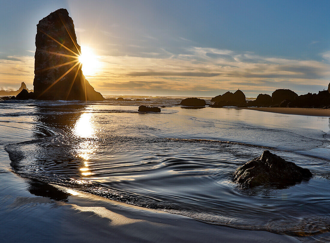 USA, Oregon. Cannon Beach: Ebbe und Wellen im Sand und Meeresstapel bei Sonnenuntergang.