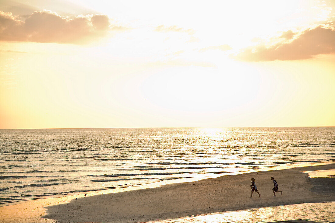 Two Children Running On Beach At Sunset