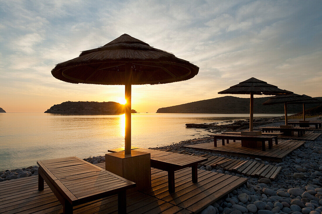 Griechenland, Kreta, Sonnenschirm und Sonnenliege am Strand gegenüber der Insel Spinalonga in der Morgendämmerung; Insel Spinalonga