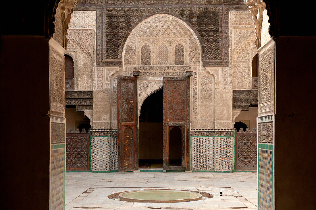 Colourful patterned tile walls in a courtyard and wooden double doors; Fez, Morocco