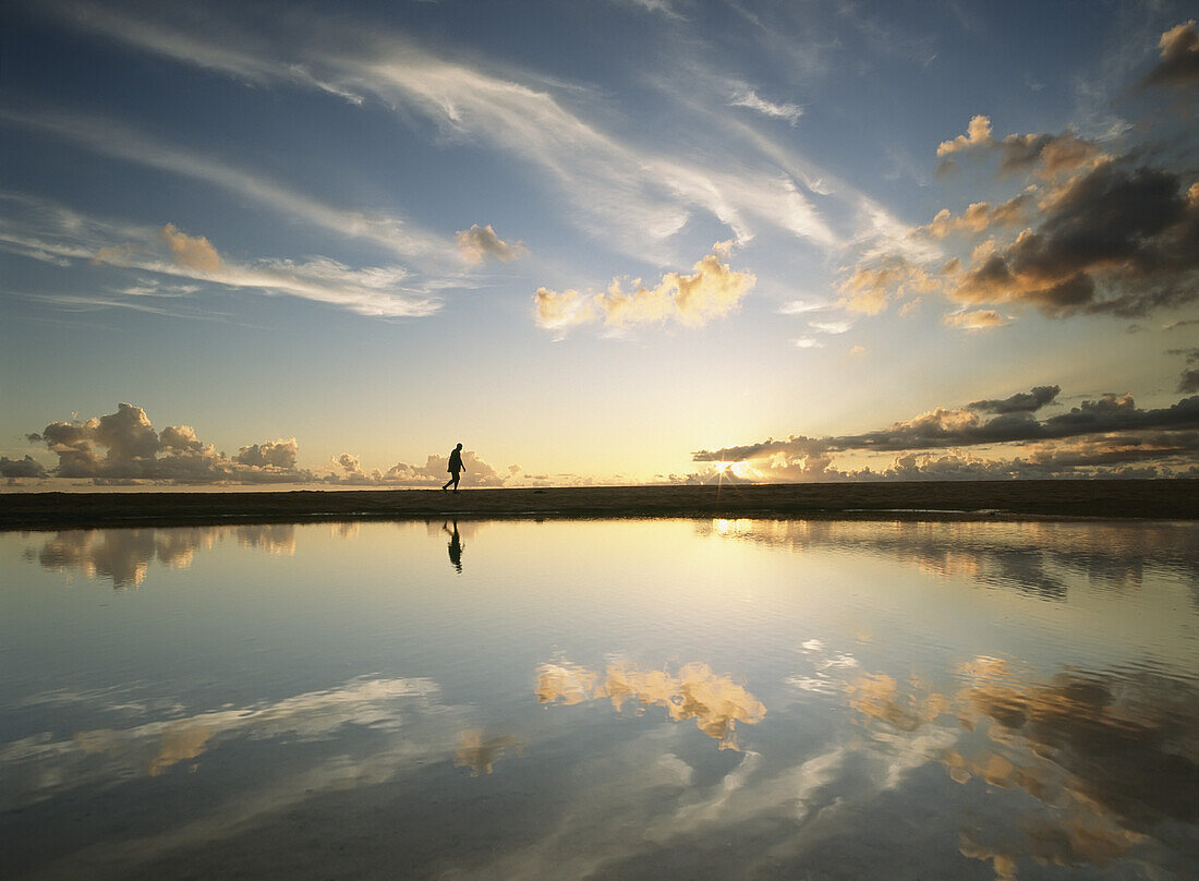 Man Walking Past Shallow Pool Beside Brighton Beach On West Coast Of Barbados At Dusk.