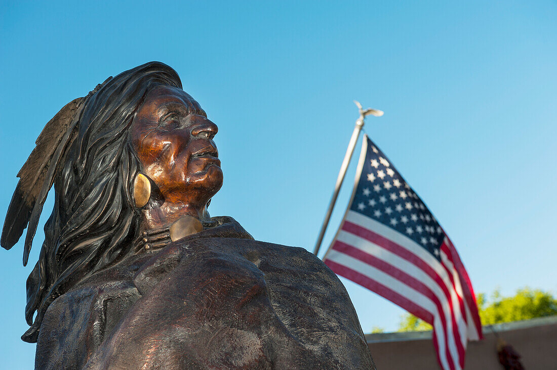Bronzestatue eines Indianers neben einer amerikanischen Flagge beim Friday Night Canyon Road Gallery Walk in Santa Fe, New Mexico, USA