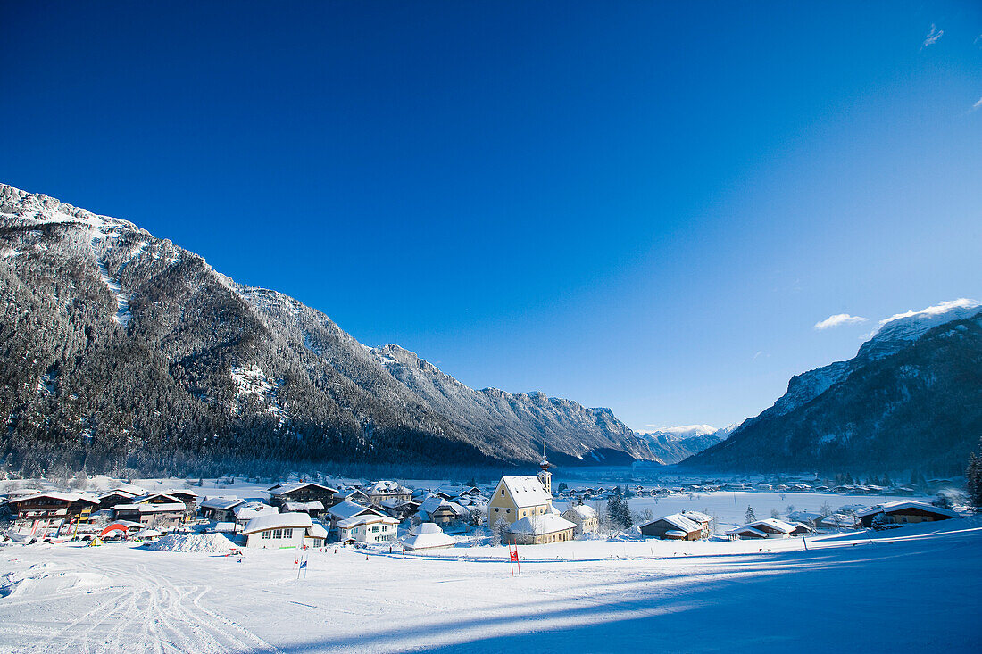 Schneebedecktes Dorf mit Bergen und malerischer Kirche in einem Tal unterhalb der Skipisten in Waidring, Österreichische Alpen, Österreich