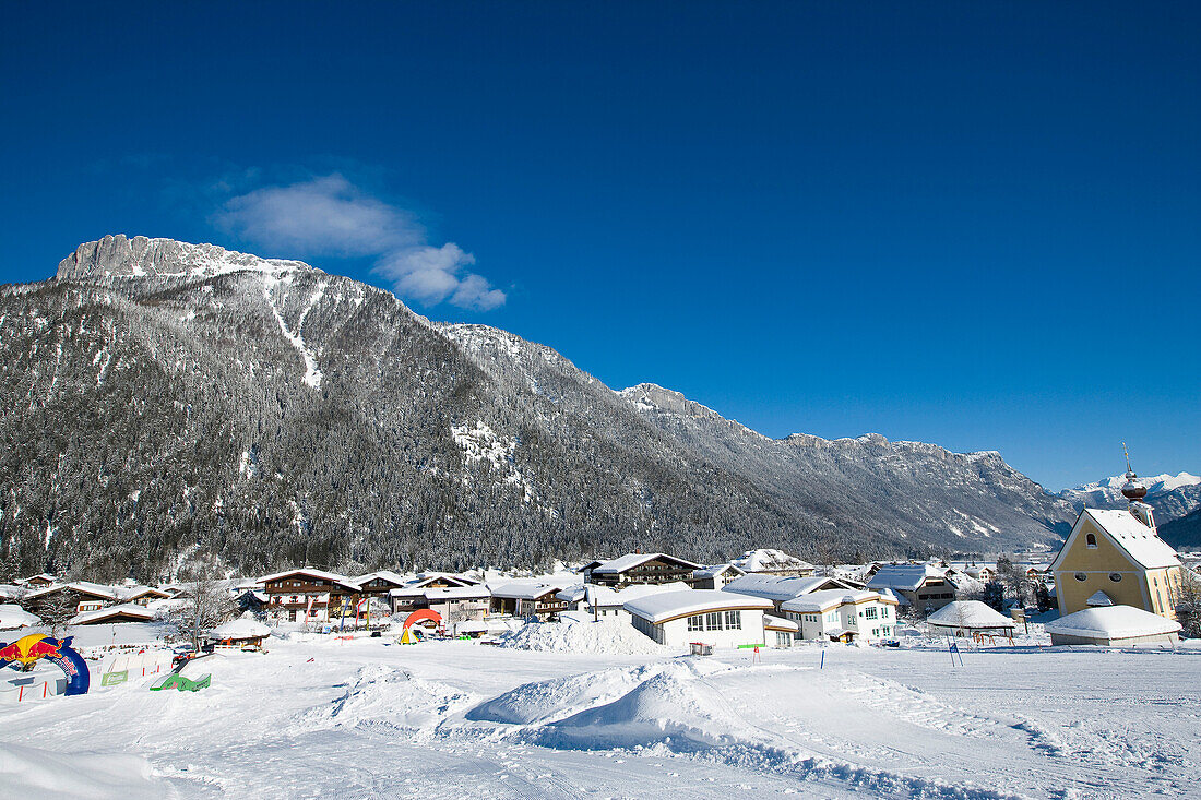 Schneebedecktes Dorf mit Bergen und malerischer Kirche in einem Tal unterhalb der Skipisten in Waidring, Österreichische Alpen, Österreich