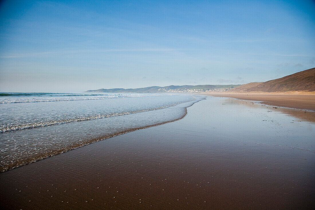 Wellenplätschern am Sandstrand, an einem ruhigen sonnigen Tag in Putsborough Sands, Nord-Devon, Großbritannien