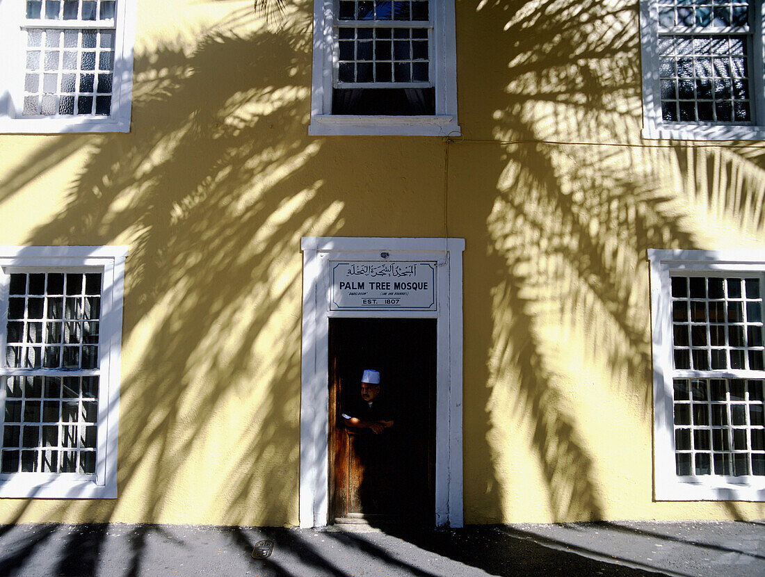 Muslimischer Mann steht im Schatten einer Palme vor der Tür der Palm Tree Moschee, Long Street, Kapstadt, Südafrika.