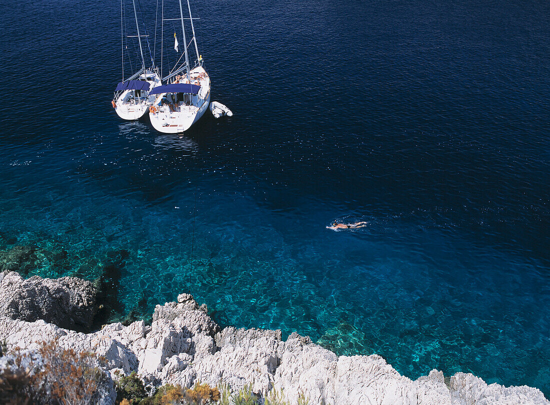 Mann schnorchelt an zwei Yachten vorbei, die in einer kleinen Bucht auf der Insel Bisevo vor Vis, Kroatien, festgemacht haben.