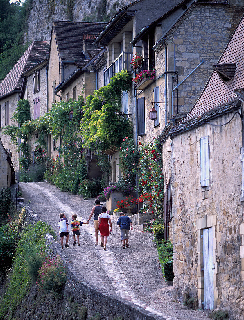 Familie beim Spaziergang entlang einer kleinen Straße im Dorf Benac, Region Dordogne, Frankreich.