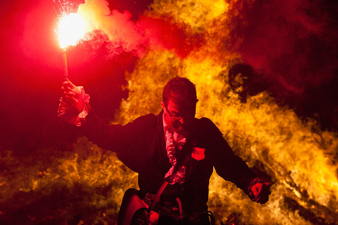 Als Pirat verkleideter Mann von der Southover Bonfire Society vor einem großen Lagerfeuer mit roter Fackel, Bonfire Night, Lewes, East Sussex, Großbritannien