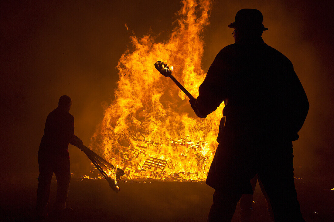 Silhouettes Of People Preparing To Throw Burning Torches On Large Bonfire At Barcombe Bonfire Night, Barcombe, East Sussex, Uk