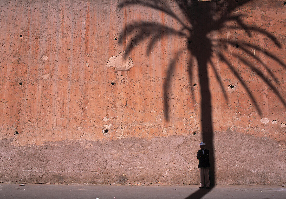 Mann steht im Schatten der Dattelpalme auf der alten Stadtmauer von Marrakesch, Marokko.