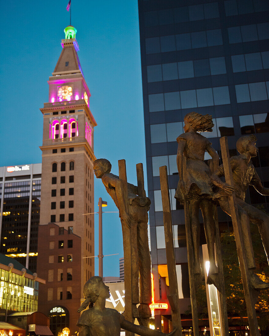 USA, Colorado, Bronze sculpture of children playing on stilts situated on 16th Street mall at night; Denver