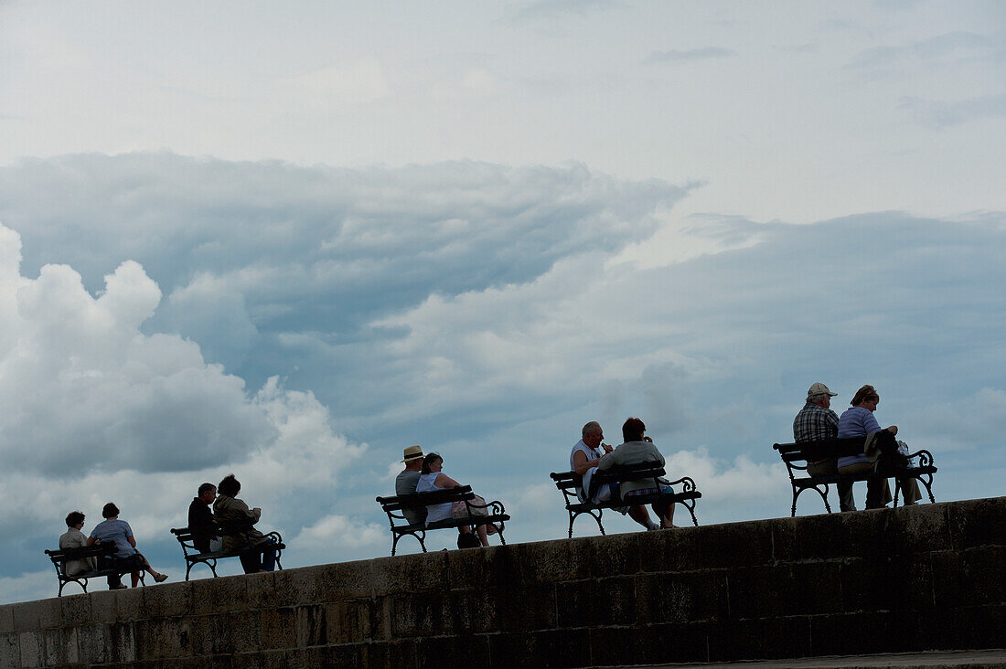 Croatia, Silhouettes of couples sitting on benches on sea wall; Dubrovnik