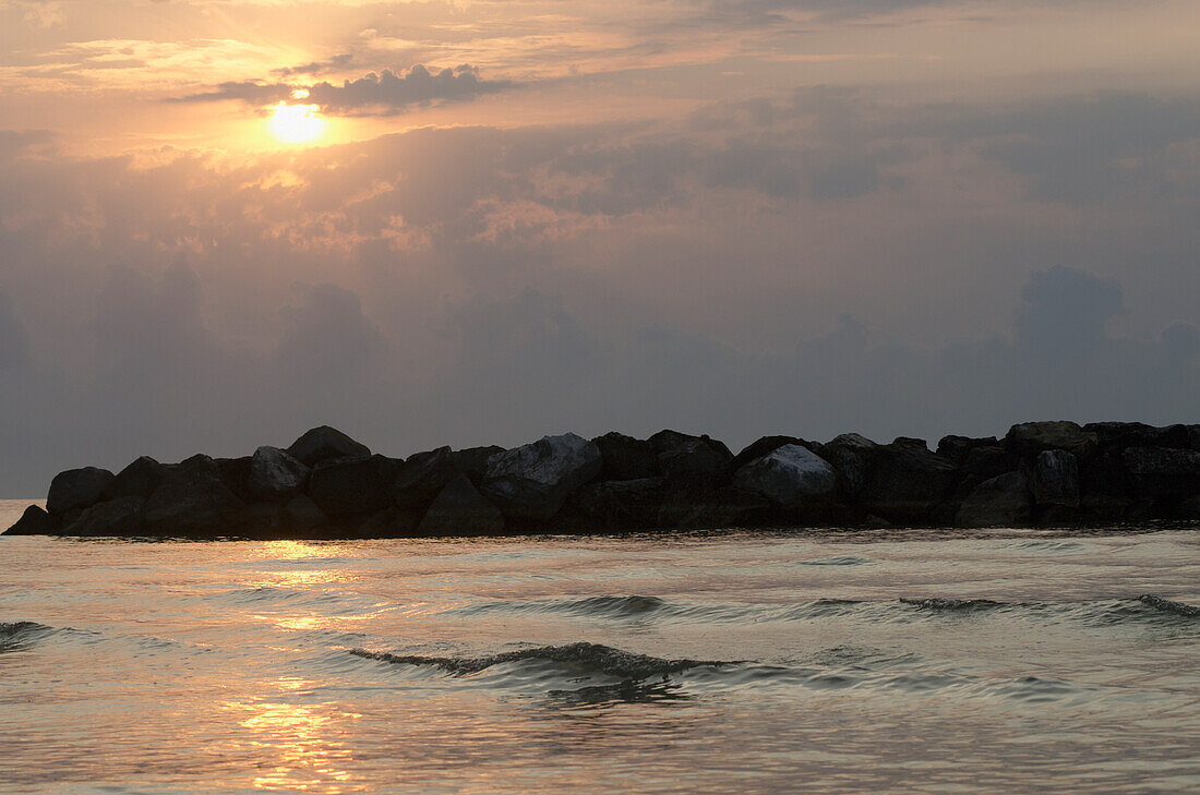 Italy, Marche, Sunrise on Adriatic sea with rocks and clouds; Porto San Giorgio