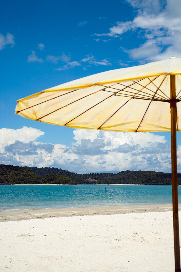 Sonnenschirm am Strand mit Blick aufs Meer und kleiner Insel im HintergrundPantai Cenang (Cenang Beach), Pulau Langkawi, &#10; Malaysia, Südostasien.