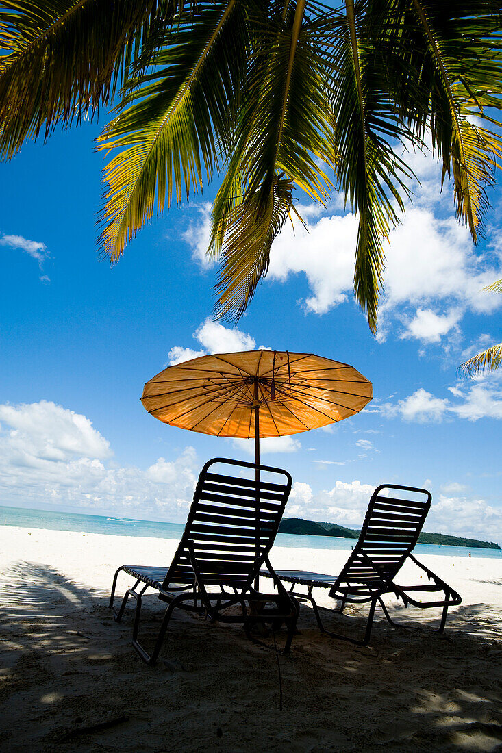Liegestühle unter Sonnenschirm am weißen Sandstrand mit Palmen mit Blick auf das blaue Meer. Pantai Cenang (Cenang Beach), Pulau Langkawi, &#10; Malaysia, Südostasien.