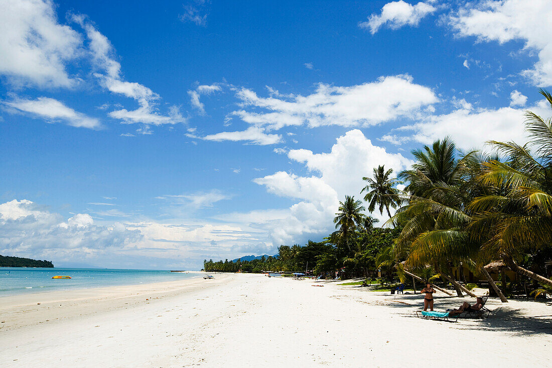 Malaysia, Pantai Cenang (Cenang beach); Pulau Langkawi, blue skies and islands in background, White sandy beach with palm trees