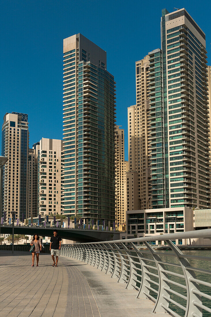 UAE, People walking through Dubai Marina area with large residential blocks of flats behind; Dubai