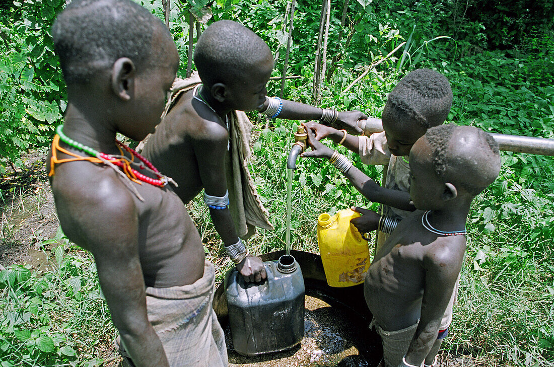 Gruppe von Mursi Stammeskindern holt Wasser aus einem von christlichen Missionaren (Serving in Mission) gegrabenen Brunnen. Makki / Süd-Omo / Region der südlichen Nationen, Nationalitäten und Völker (Äthiopien).