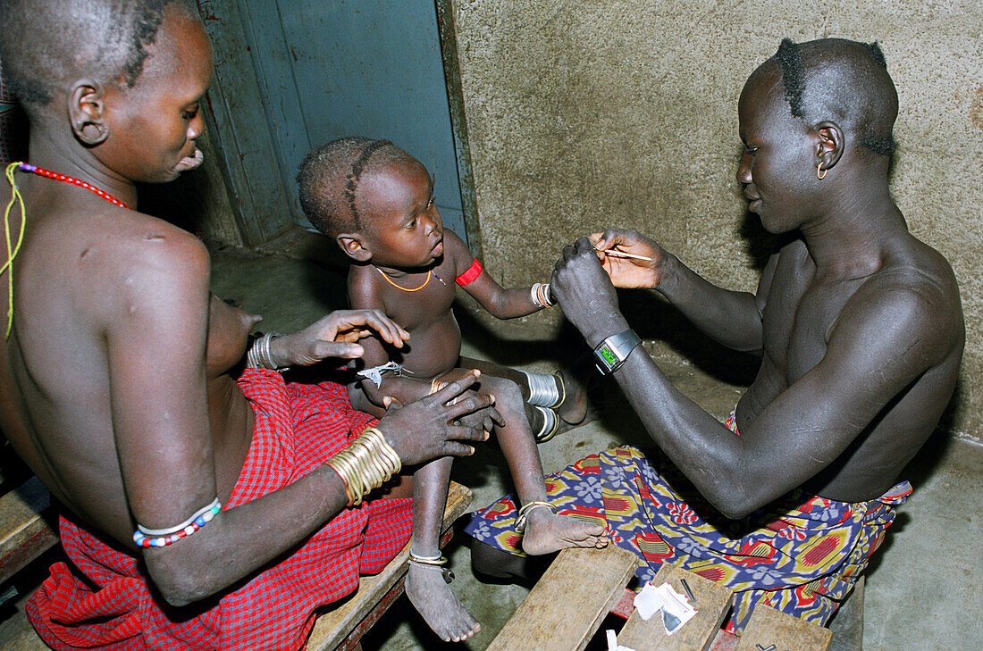 Ein Mursi-Stammesangehöriger, der als Hilfskrankenpfleger für christliche Missionare arbeitet, führt einen Malaria-Test an einem kleinen Kind durch. Makki / Süd-Omo / Region der südlichen Nationen, Nationalitäten und Völker (Äthiopien).