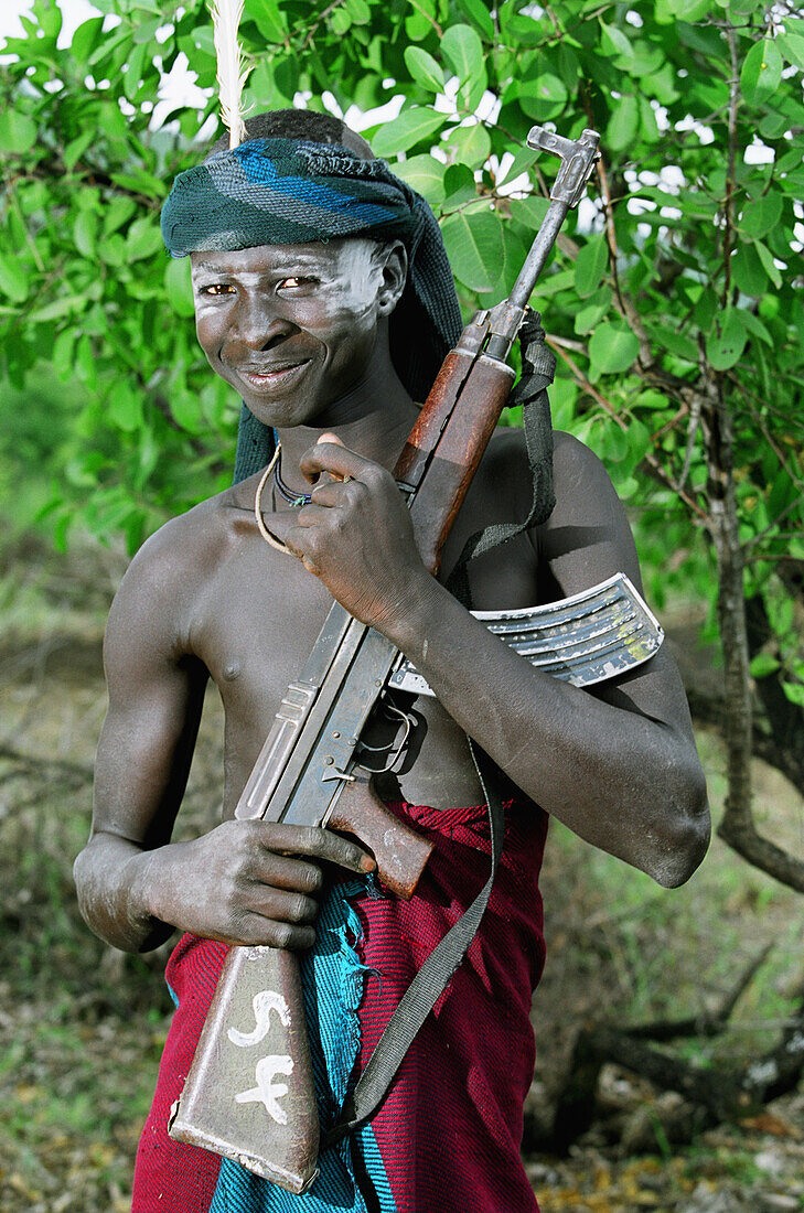 Young Mursi tribal man posing with an AK-47 Kalashnikov machine gun (a weapon & a new symbol of Mursi identity & social status) which found their way into the area during the Second Civil War in Sudan (1983 â€“ 2005). Makki / South Omo / Southern Nations, Nationalities & People's Region (Ethiopia).