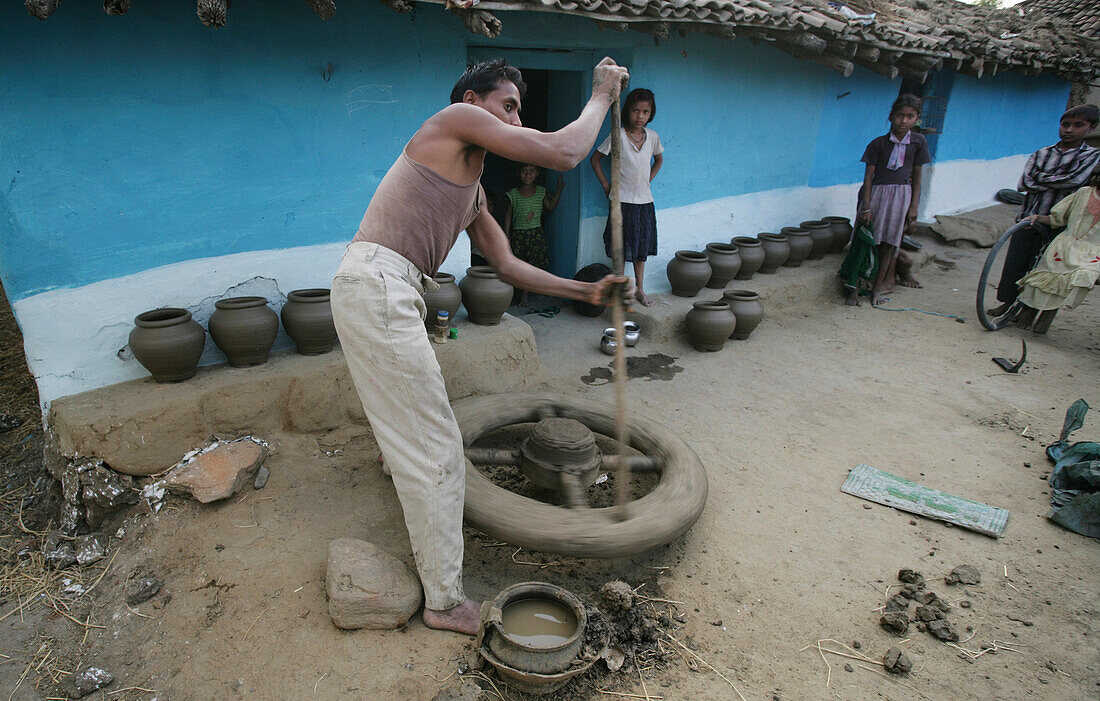 Mann arbeitet an einer Töpferscheibe, während seine Familienmitglieder zusehen, Töpferdorf; Madhya Pradesh, Indien