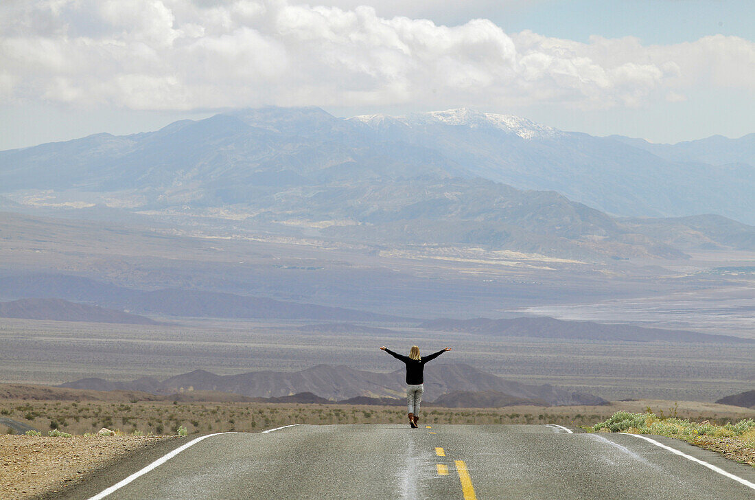 USA, Grenze Nevada, Kalifornien, Route 374; Death Valley National Park, Highway 374, Junge Frau auf verlassener Straße in der Wüste stehend