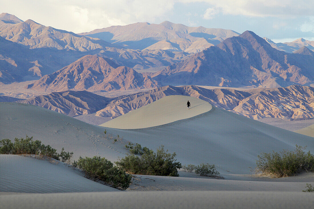 Usa, California, Young Woman Walking On Mesquite Flat Sand Dunes With Amargosa Range Mountains In Background; Death Valley National Park