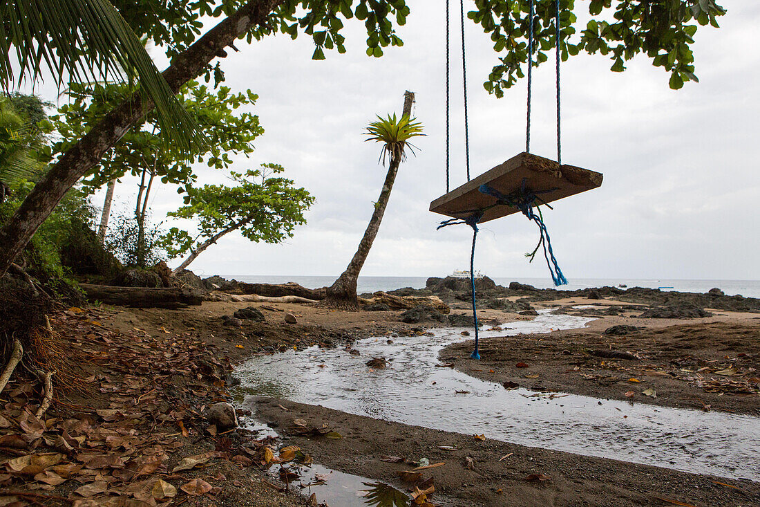 Im Caletas-Reservat auf der Halbinsel Osa hängt eine Holzschaukel von einem Baum über einem kleinen Bach, der ins Meer mündet; Costa Rica