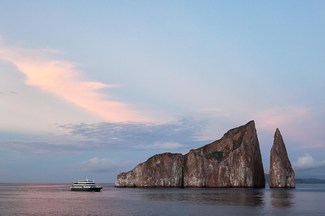 An expedition vessel passes near a large rock formation.; Pacific Ocean, Galapagos Islands, Ecuador