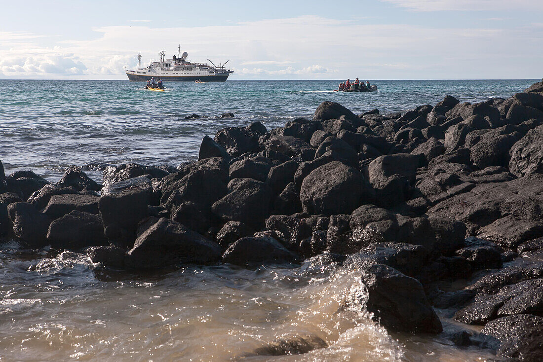 Tourists in inflatable boats approach a shoreline in the Galapagos Islands.; Pacific Ocean, Galapagos Islands, Ecuador