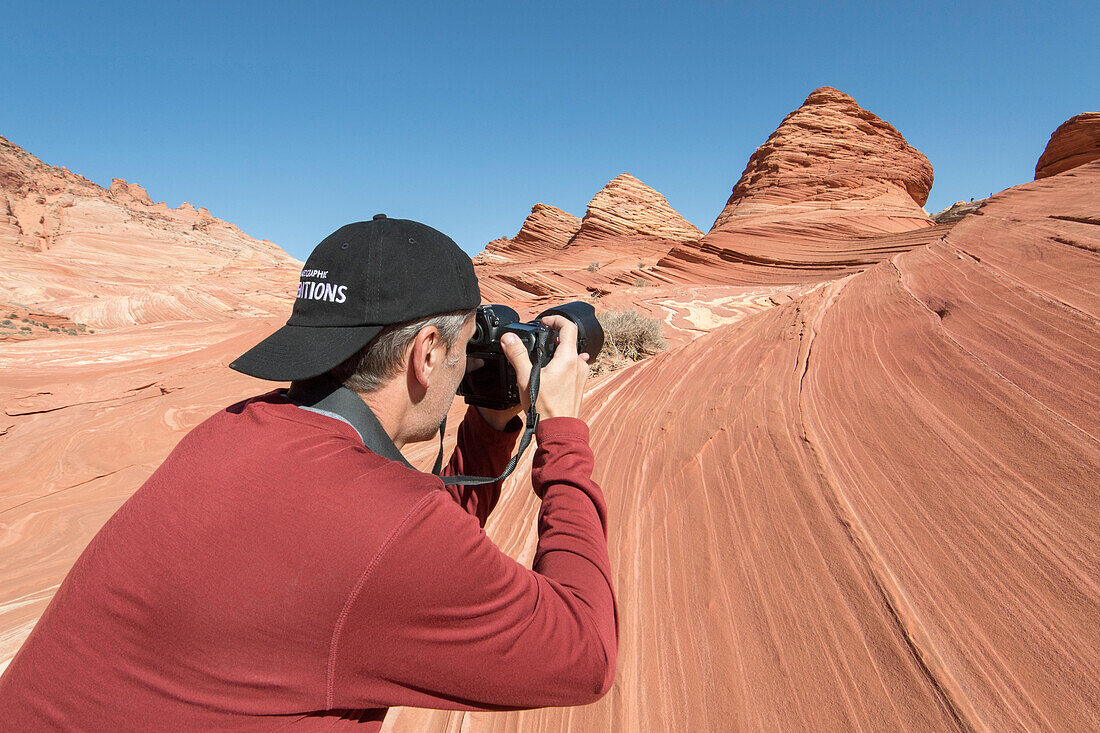 A man takes a picture of pyramid shaped sandstone formations in Coyote Buttes North.