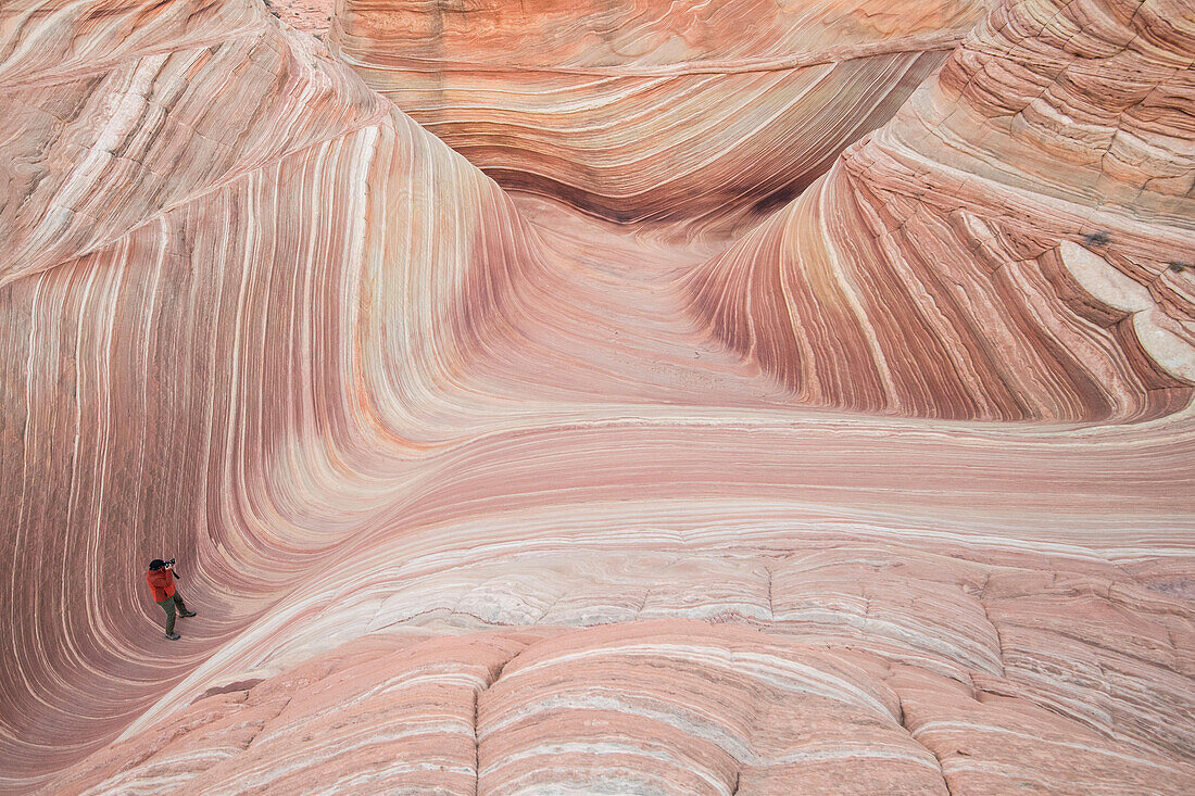 A man takes a picture of The Wave sandstone rock formation, located in Coyote Buttes North, Paria Canyon, Vermillion Cliffs Wilderness.