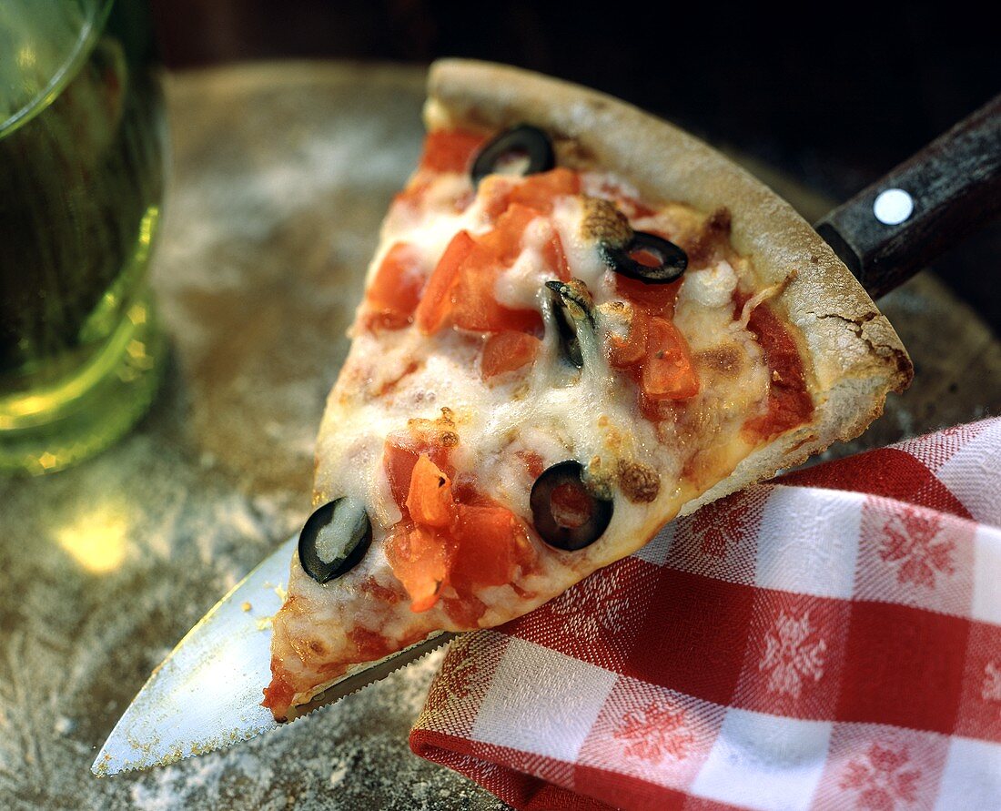 Ein Stück Pizza mit Tomaten, Käse & Oliven auf Messer