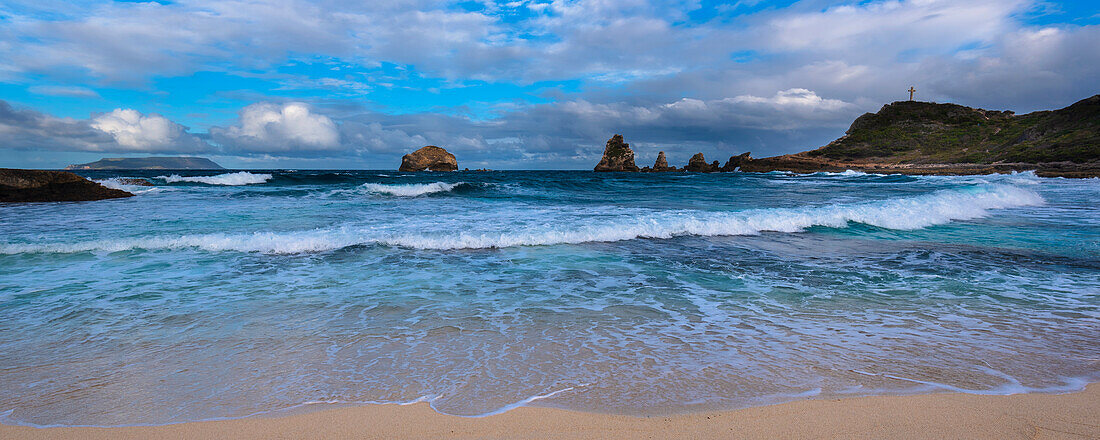 Waves and seasurf meeting the sandy beach at Grande-Terre with the Grand-Croix in the distance at the tip of Pointe des Chateaux; Guadeloupe, French West Indies