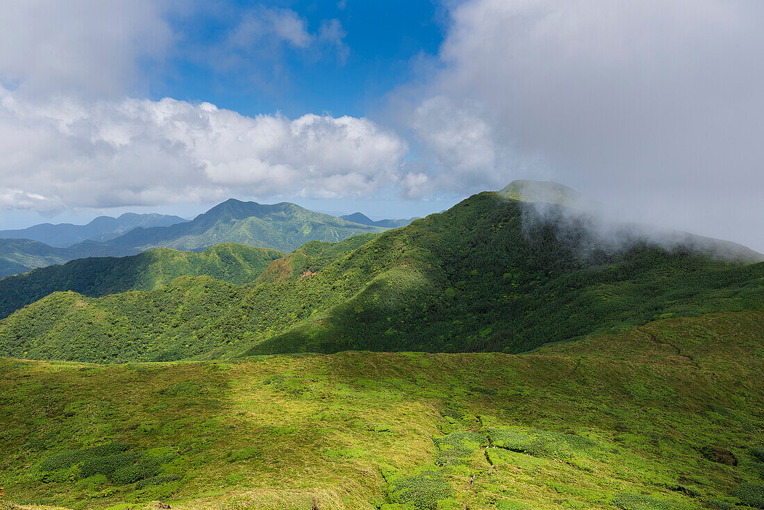 Misty clouds and mountain view from the top of La Grande Soufriere, an active stratovolcano on Basse-Terre with people hiking through the dense jungle; Guadeloupe, French West Indies