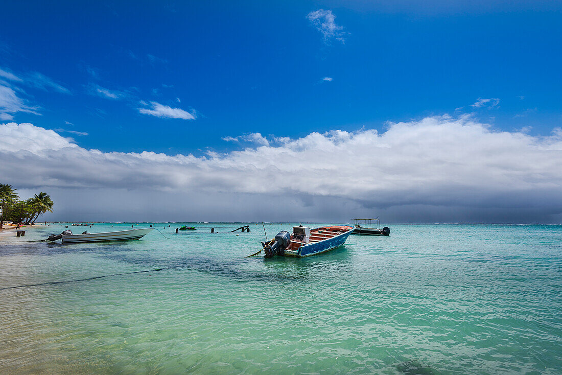 Am Strand von Sainte-Anne auf Grande-Terre sind Motorboote im türkisfarbenen Wasser der Karibik vertäut, während sich am Horizont Regenwolken bilden; Guadeloupe, Französische Westindische Inseln