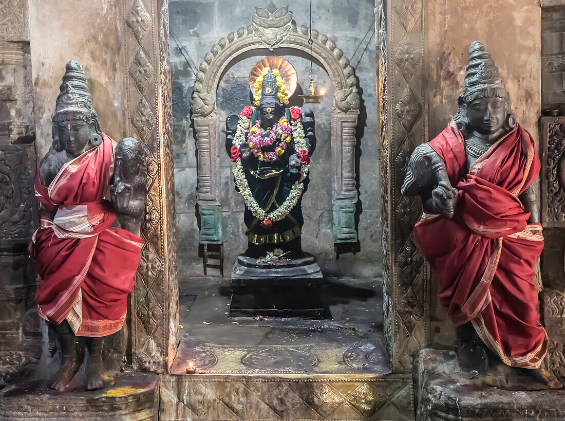 Alcove with Hindu deity statue in wall with guardian statues wrapped in silk on either side at the Dravidian Chola era Airavatesvara Temple; Darasuram, Tamil Nadu, India