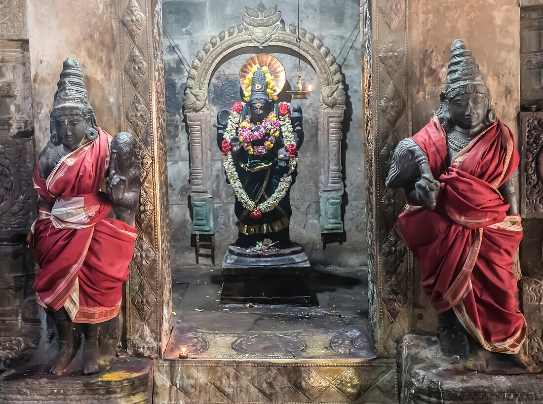 Nische mit Statue einer Hindu-Gottheit in der Wand mit in Seide gehüllten Wächterstatuen auf beiden Seiten im Airavatesvara-Tempel aus der dravidischen Chola-Zeit; Darasuram, Tamil Nadu, Indien